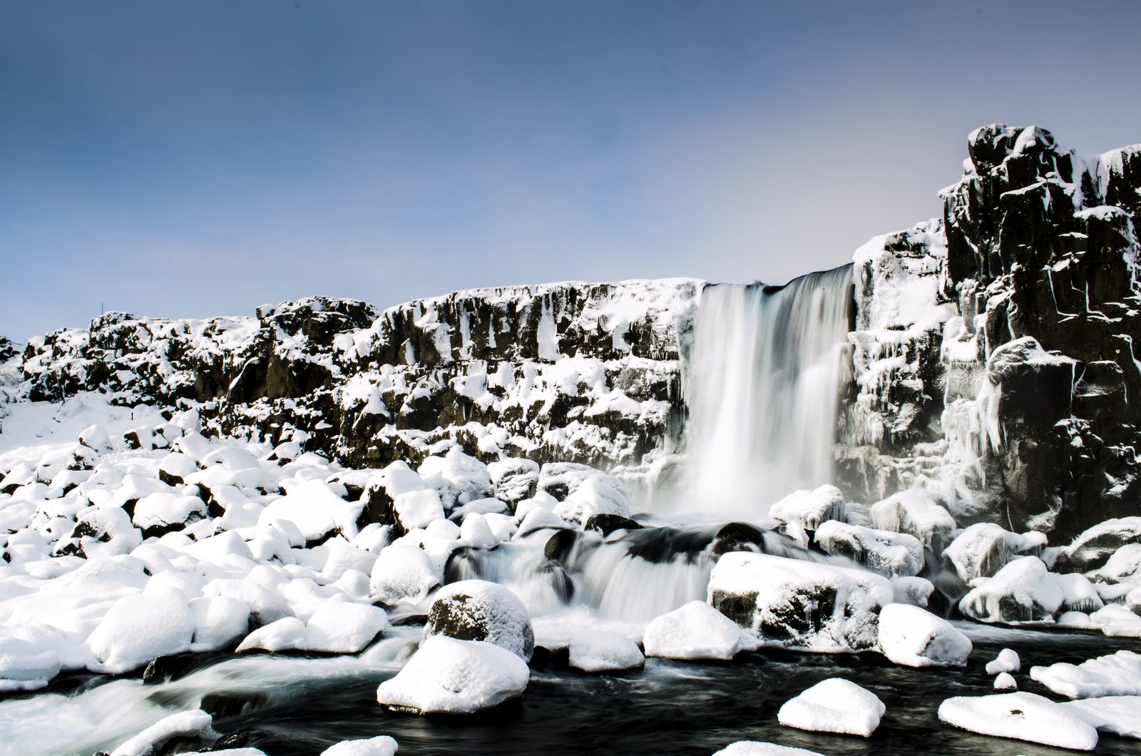Der Wasserfall Öxarárfoss in Island, umgeben von schneebedeckten Felsblöcken