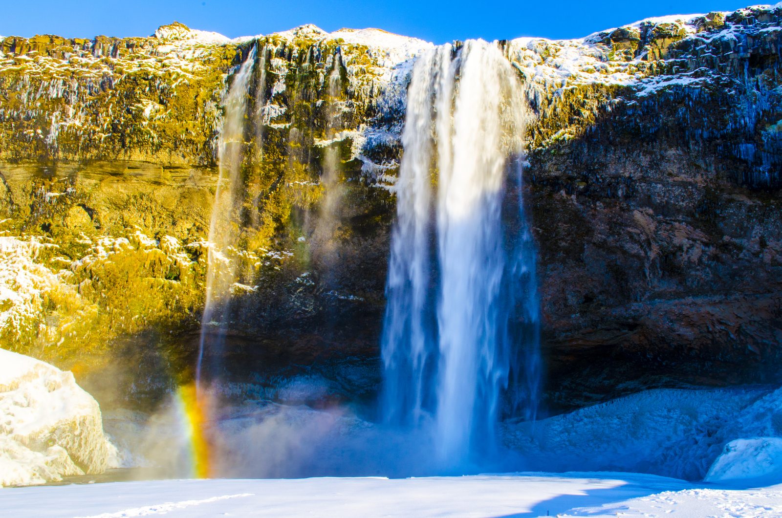 Wasserfall Seljalandsfoss im Winter mit einem Regenbogen in der Gischt