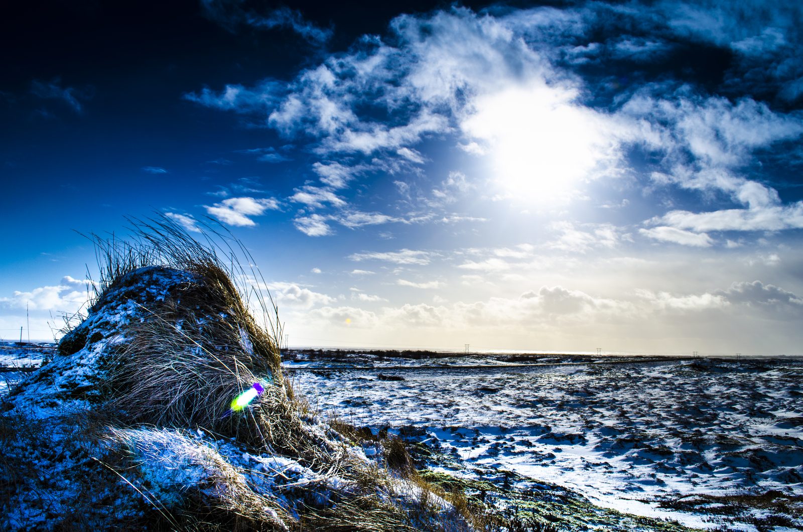 Verschneite Küstenlandschaft in Island unter einem dramatischen blauen Himmel mit Sonne